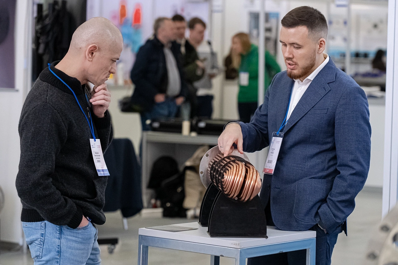 A company representative demonstrating equipment with a copper coil to a visitor at the Climate World exhibition.